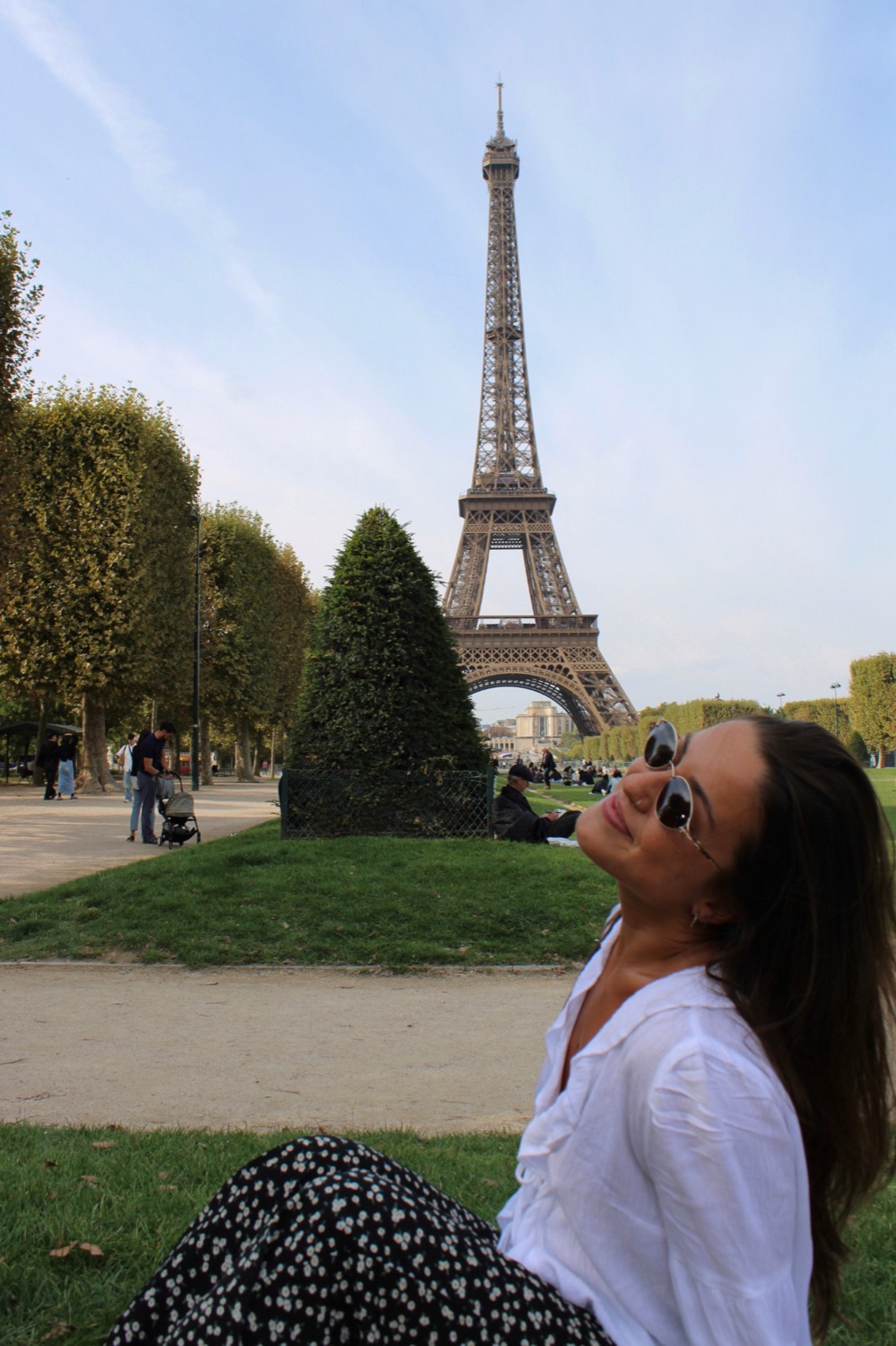 Gabi sentada no gramado com a Torre Eiffel ao fundo